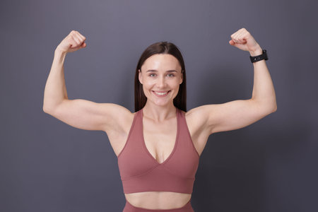 Woman in fitness clothes showing her biceps on grey background