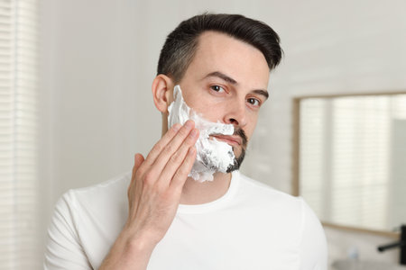 Handsome man applying shaving foam in bathroomの写真素材