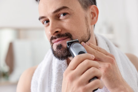 Handsome man shaving with trimmer at home, closeup