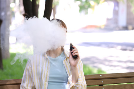 Young woman using electronic smoking device outdoors. Space for text