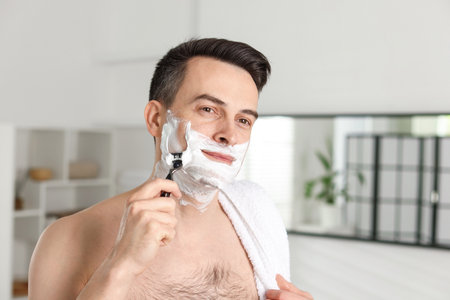 Handsome man shaving with razor at homeの写真素材