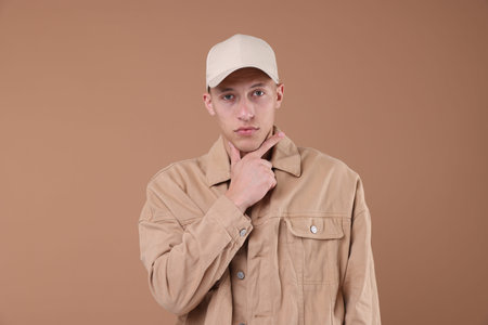 Young man wearing stylish beige baseball hat on light brown background