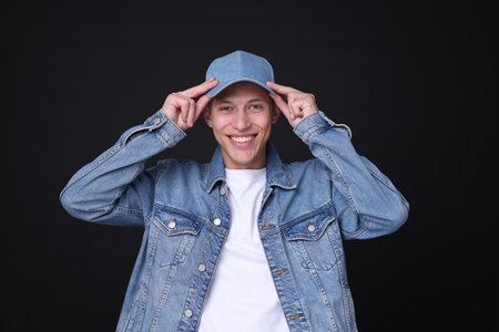 Young man wearing stylish denim baseball hat on black backgroundの写真素材