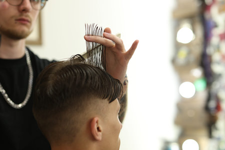 Professional barber making stylish haircut in barbershop, closeup. Space for text