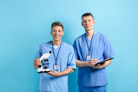 Medical students with microscope and clipboard on light blue backgroundの写真素材