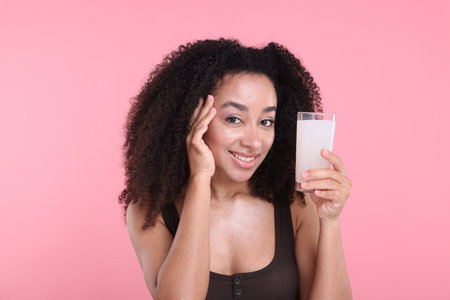 Beautiful Brazilian woman with glass of collagen water on pink backgroundの写真素材