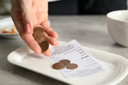 Woman putting tips onto plate at gray table in cafe, closeup