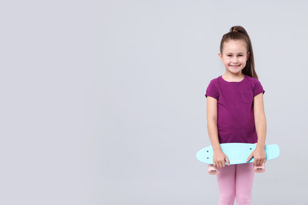 Little girl with penny board on light grey background, space for textの写真素材