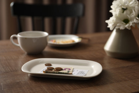 Tips, receipt, chrysanthemum flowers, dirty plate and cup on wooden table in cafe, closeup