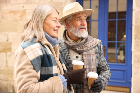 Happy elderly couple with coffee cups walking on city streetの写真素材