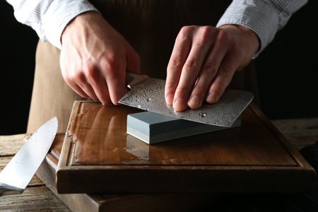 Man sharpening knife with sharpener on wooden table, closeupの写真素材