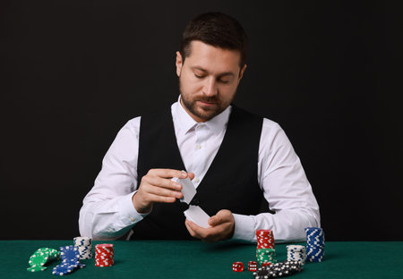 Professional croupier shuffling cards at gambling table against black background