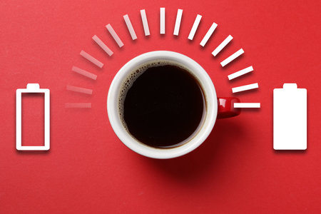 Cup of coffee and energy gauge on red background, top view. Low level battery becoming fully charged after caffeine consumptionの写真素材