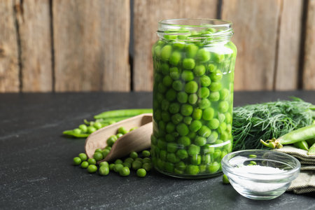 Fresh green peas in pickling jar, dill, pods and salt on black table, closeup. Space for textの写真素材