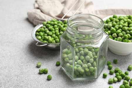 Fresh green peas and pickling jar on light gray table, closeupの写真素材