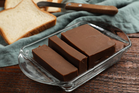 Tasty chocolate butter, slices of bread and knife on wooden table, closeup