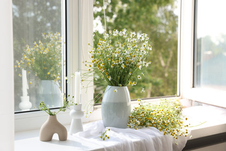 Beautiful chamomile flowers and candle on window sill indoorsの写真素材