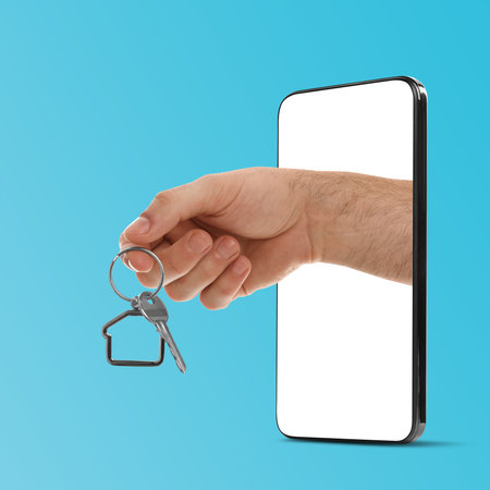 Man's hand with key sticking out from smartphone on light blue background. Real estate services onlineの写真素材