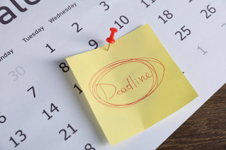 Sticky note with word Deadline and calendar on wooden table, closeupの写真素材