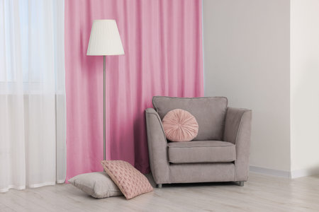 Comfortable armchair and floor lamp near window with pink curtains in room. Interior designの写真素材