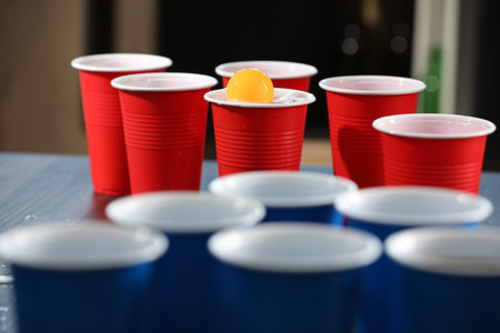Beer pong game. Plastic cups with drinks and ball on table, closeupの写真素材