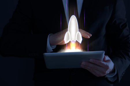 Business, successful startup. Man using tablet computer against dark background, closeup. Rocket...