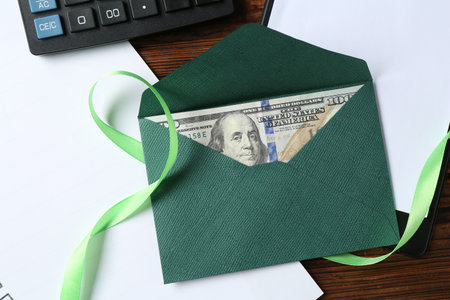 Money bonus. Envelope with dollar banknote, clipboard, ribbon and calculator on wooden table, flat layの写真素材