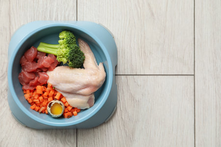 Feeding bowl with natural raw products for pet on white wooden floor, top view. Space for textの写真素材