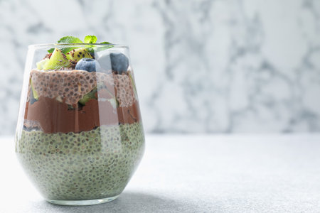 Delicious chocolate pudding with chia seeds, kiwi, mint and blueberries in glass on gray textured table against marble background, closeup. Space for textの写真素材