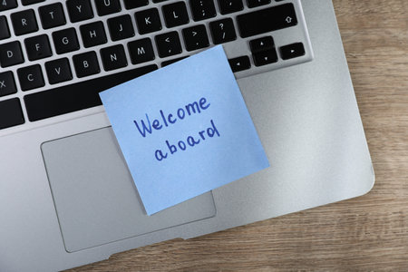 Paper note with words Welcome Aboard and laptop on wooden table, top viewの写真素材