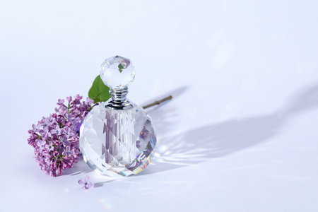 Perfume bottle and branch with lilac flowers on light gray background, closeup. Space for text