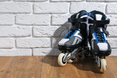 Pair of roller skates on wooden table near white brick wall, space for text