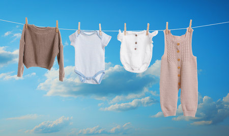 Different baby clothes drying on washing line against blue skyの写真素材