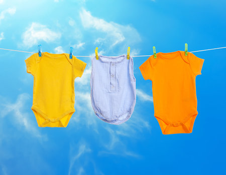 Different baby clothes drying on washing line against blue skyの写真素材