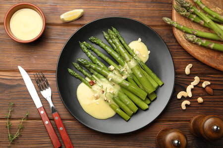 Tasty cooked asparagus served with sauce on wooden table, flat layの写真素材