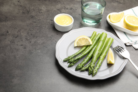 Tasty cooked asparagus served with lemon on gray table, space for textの写真素材