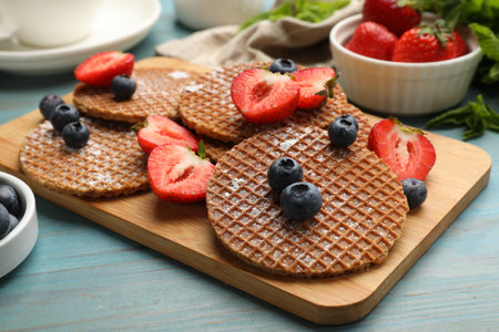 Tasty Dutch waffles (stroopwafels) and berries on light blue wooden table, closeupの写真素材