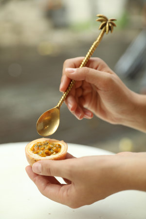 Woman eating passion fruit at table outdoors, closeup