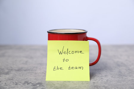 Sticky note with phrase Welcome To The Team and coffee on gray table, closeupの写真素材