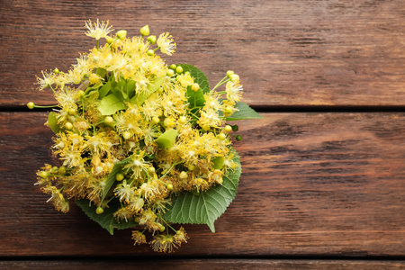 Beautiful linden flowers and green leaves on wooden table, top view. Space for textの写真素材