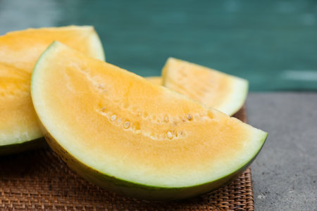 Pieces of ripe yellow watermelon on wicker table near swimming pool, closeupの写真素材