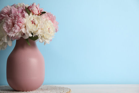 Beautiful peonies in vase on white table near light blue wall. Space for textの写真素材