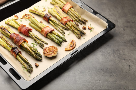 Tasty cooked asparagus with bacon and spices in baking tray on gray table, closeup. Space for textの写真素材