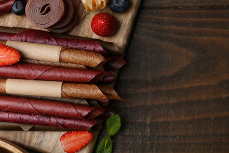 Tasty candied leather rolls, fruits and berries on wooden table, flat lay. Space for text