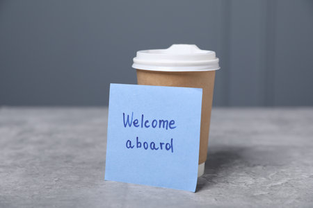 Sticky note with phrase Welcome Aboard and coffee on gray table, closeupの写真素材