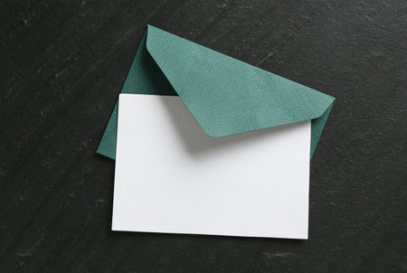 Blank invitation card and envelope on black table, top view. Space for design