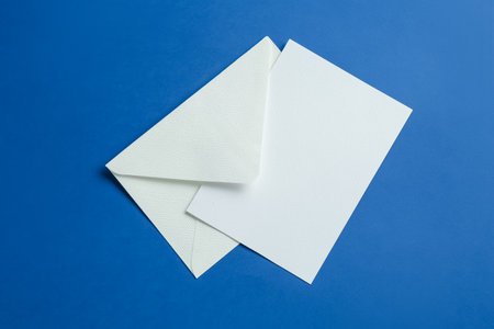 Blank invitation card and envelope on blue background, top view. Space for designの写真素材
