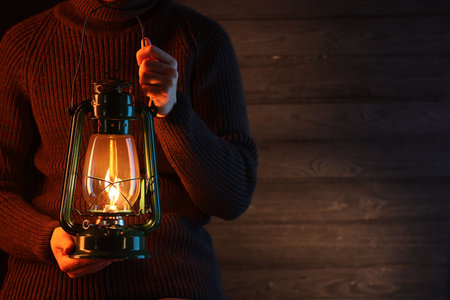 Man holding vintage kerosene lantern near wooden wall, closeup. Space for textの写真素材