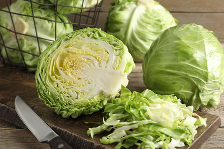 Fresh cabbages, basket and knife on wooden table, closeup