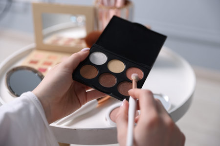 Woman with brush and eyeshadow palette at table indoors, closeup